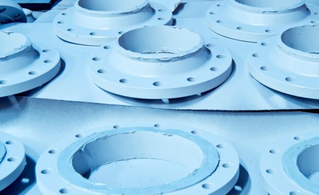 Several ceramic pipe connectors lie on pieces of cardboard. Each connector features holes on its edges.