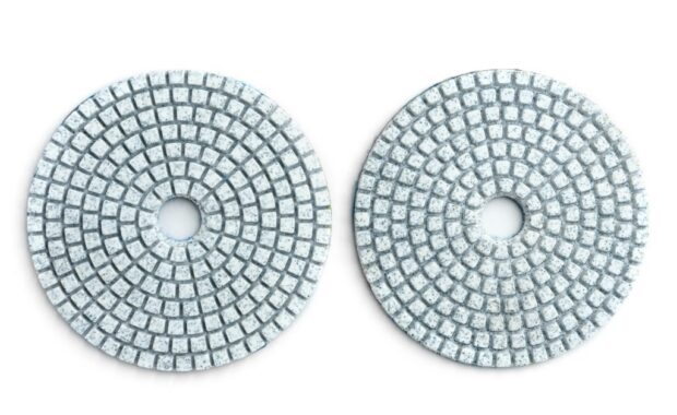 Two gray, round abrasive discs with central holes and segmented surfaces sit on a plain white background.
